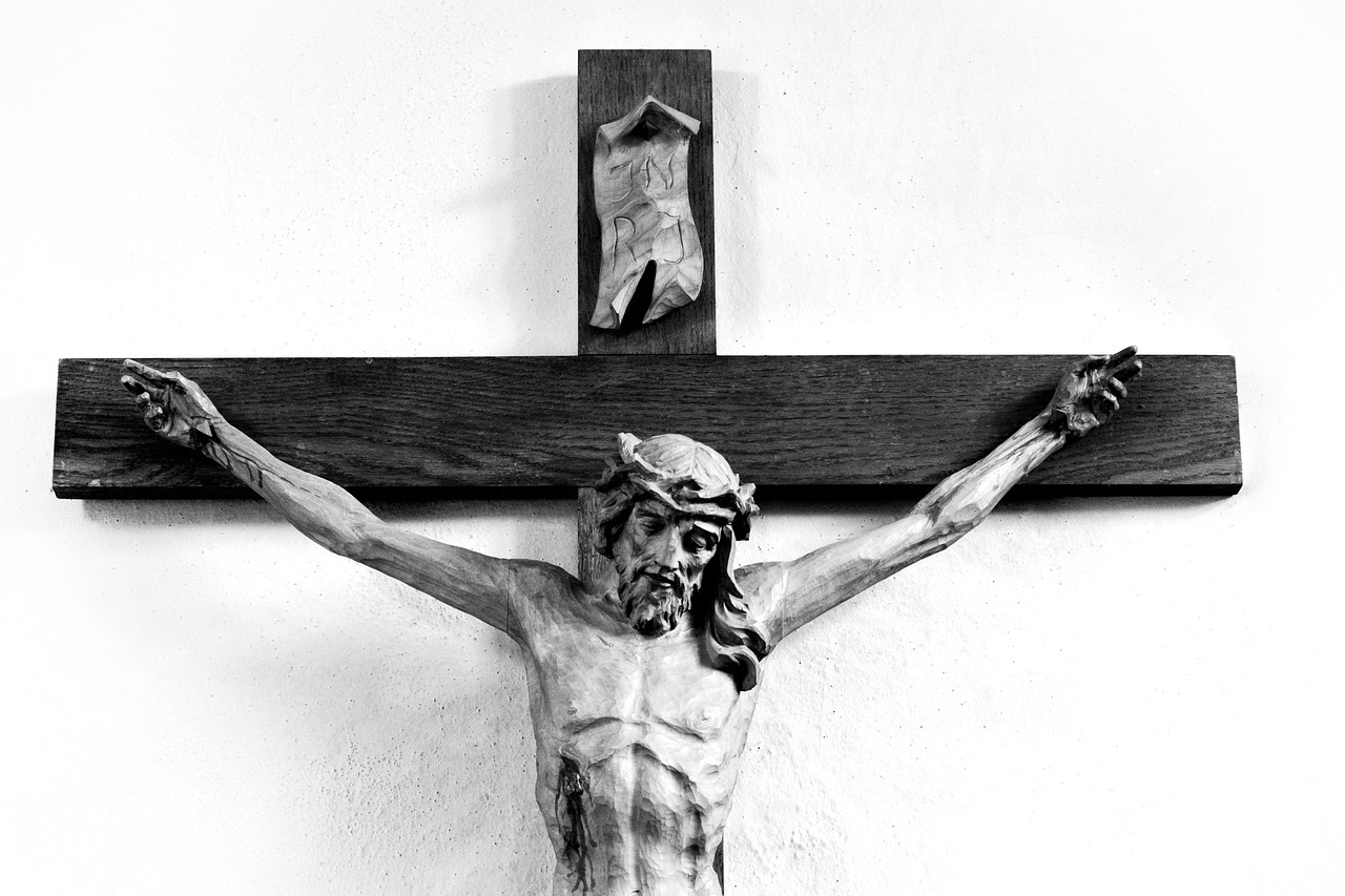 A black and white picture of the top of a crucifix of Jesus on the cross.