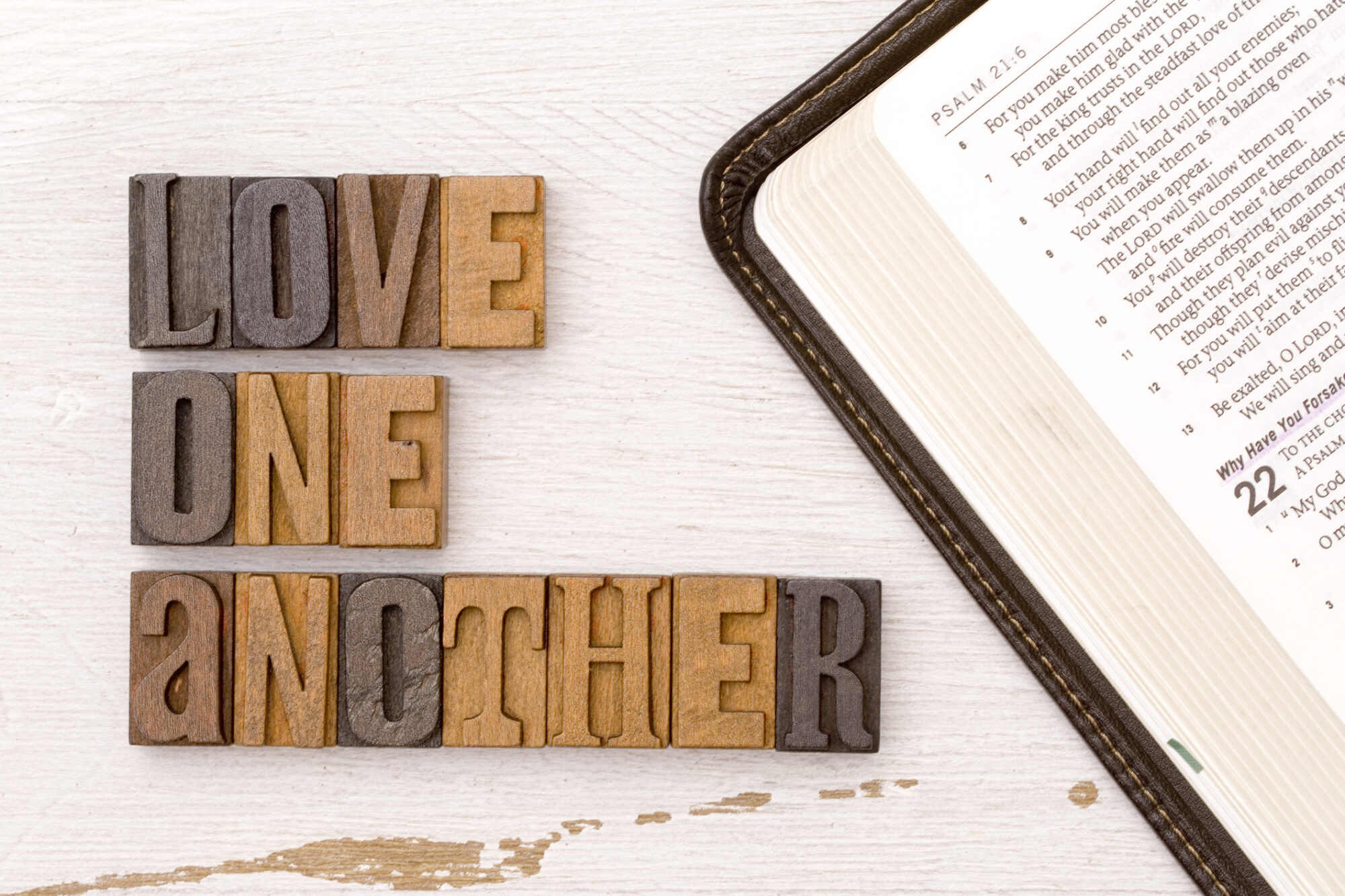 Wooden letters spell out, Love One Another by an open Bible opened to the Psalms.