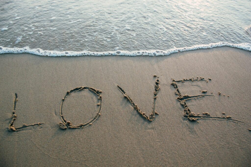 Waves rolls up on a beach where the word "love" is written in the sand.