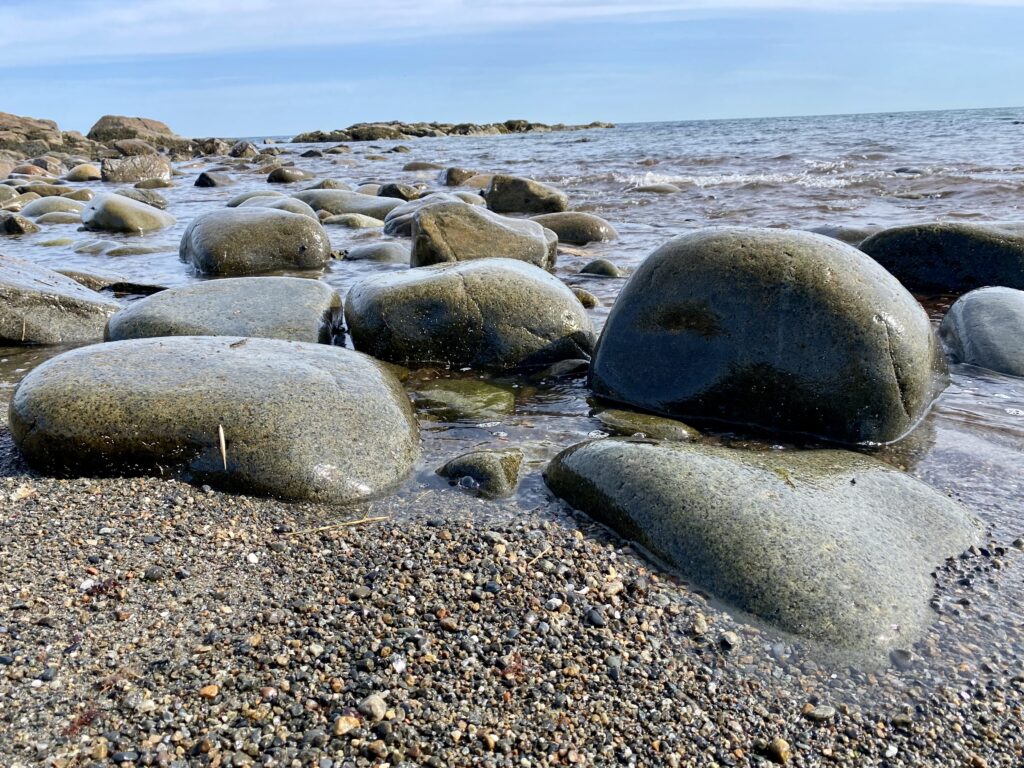 Round stones adorn the shore where the ocean and the beach meet.