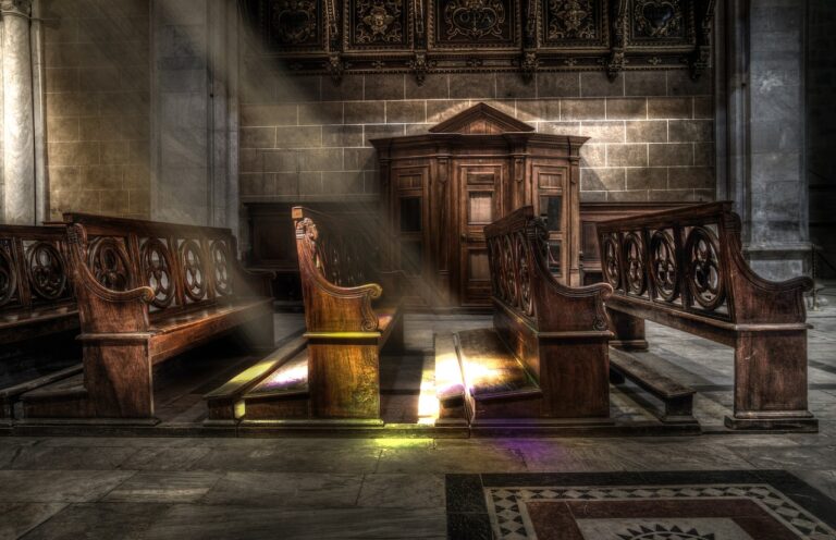 A shaft of light falls on rows of wooden pews in a side altar of a church.