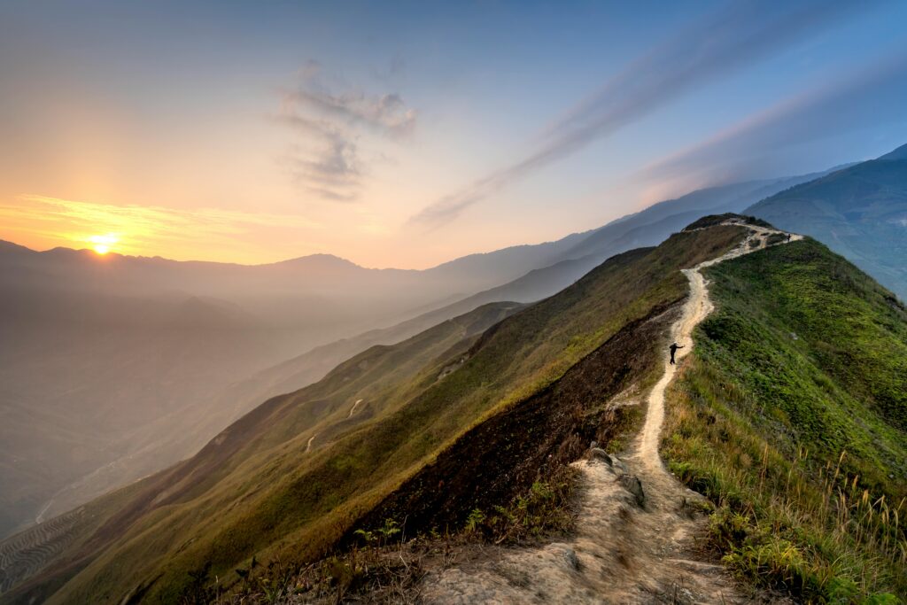 A narrow path on a high mountain with a sunrise in the background.